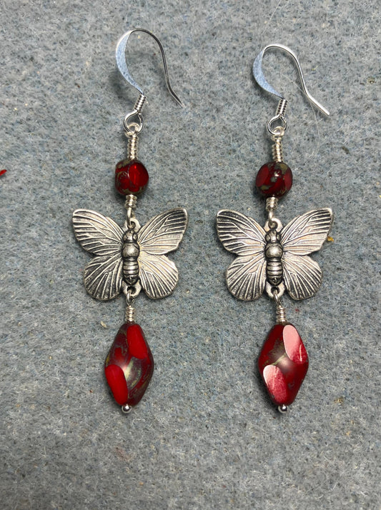 Silver butterfly connector charm earrings adorned with opaque red Czech glass twist beads and opaque red Czech glass beads.
