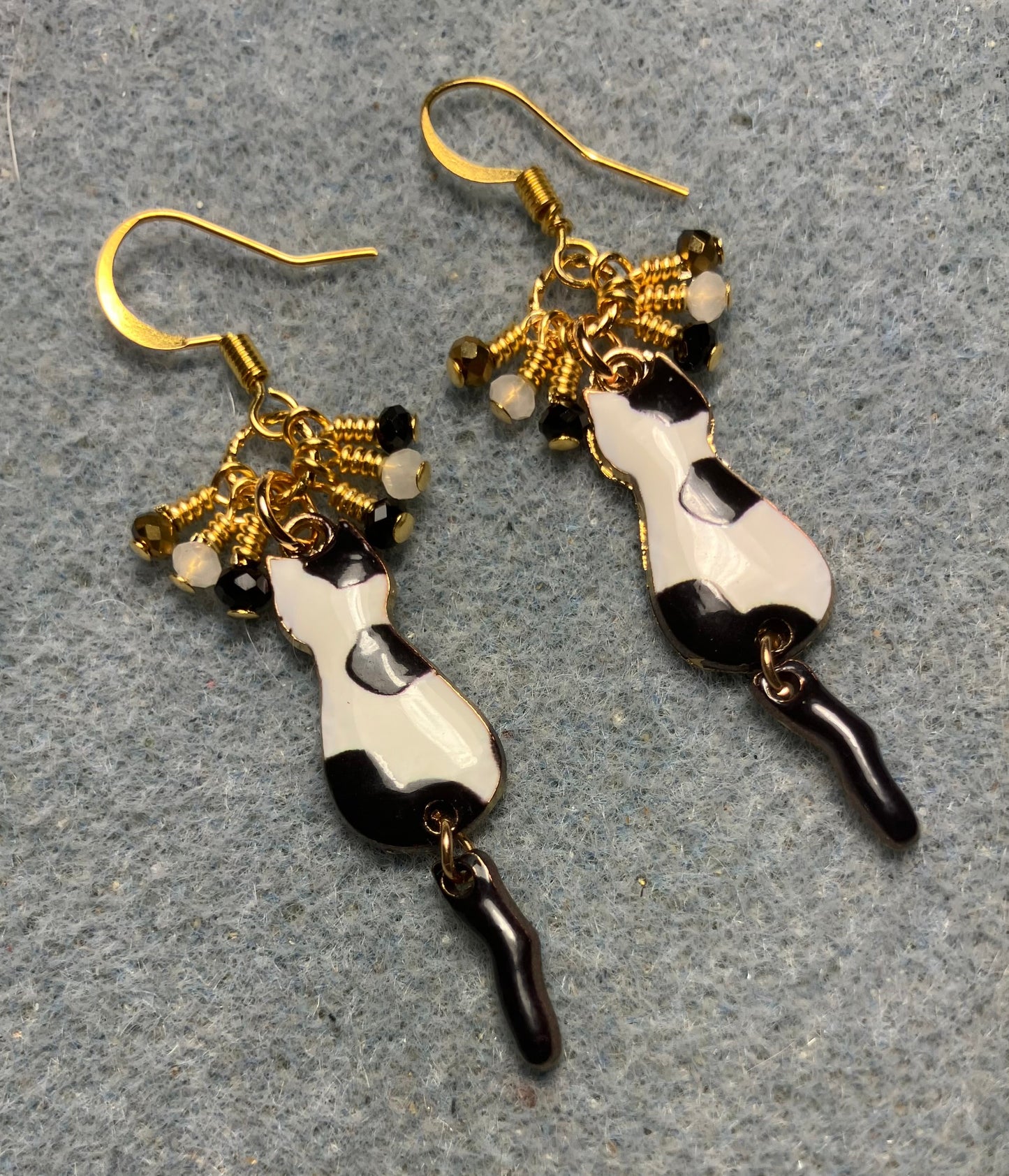 Black, white, and gold enamel cat charm earrings adorned with tiny dangling black, white, and gold Chinese crystal beads.