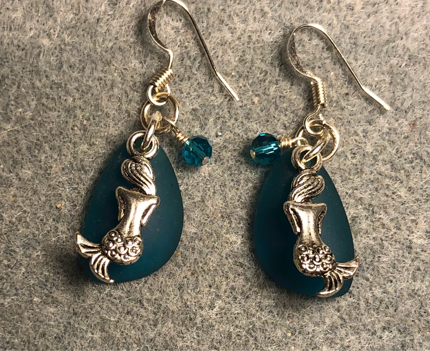 Small teal sea glass pendant bead earrings adorned with small silver mermaid charms and small teal Chinese crystal beads.