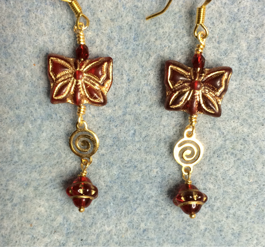 Dark red Czech glass butterfly bead earrings adorned with gold swirly connectors and dark red Czech glass Saturn beads.