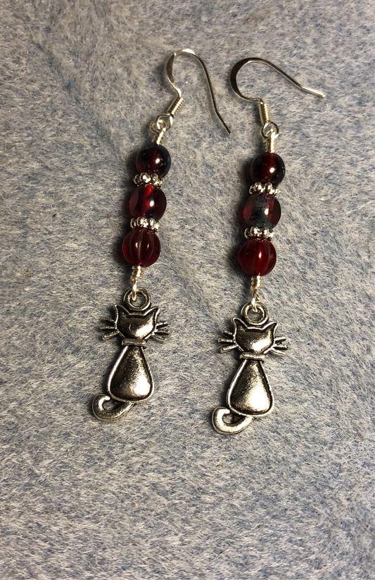 Small silver cat charm earrings adorned with dark red Czech glass beads.
