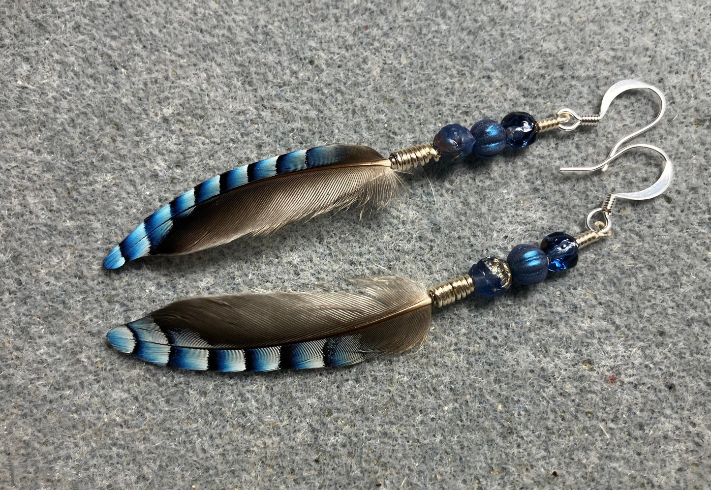 Small striped blue jay feather earrings adorned with small blue Czech glass beads.