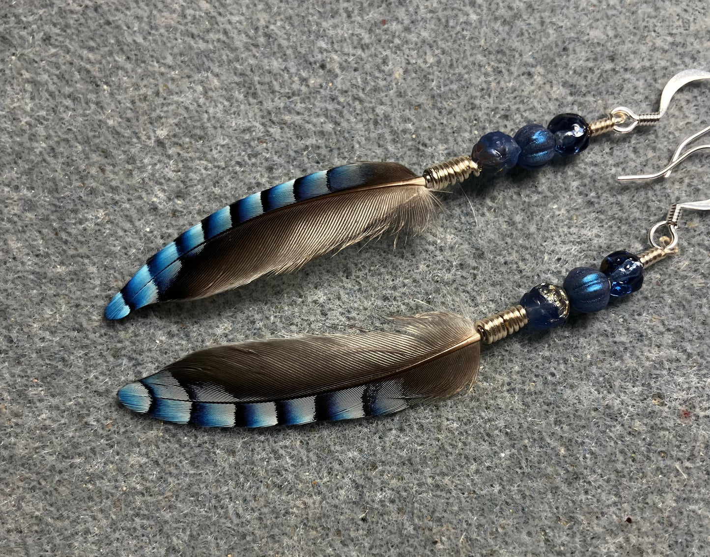 Small striped blue jay feather earrings adorned with small blue Czech glass beads.