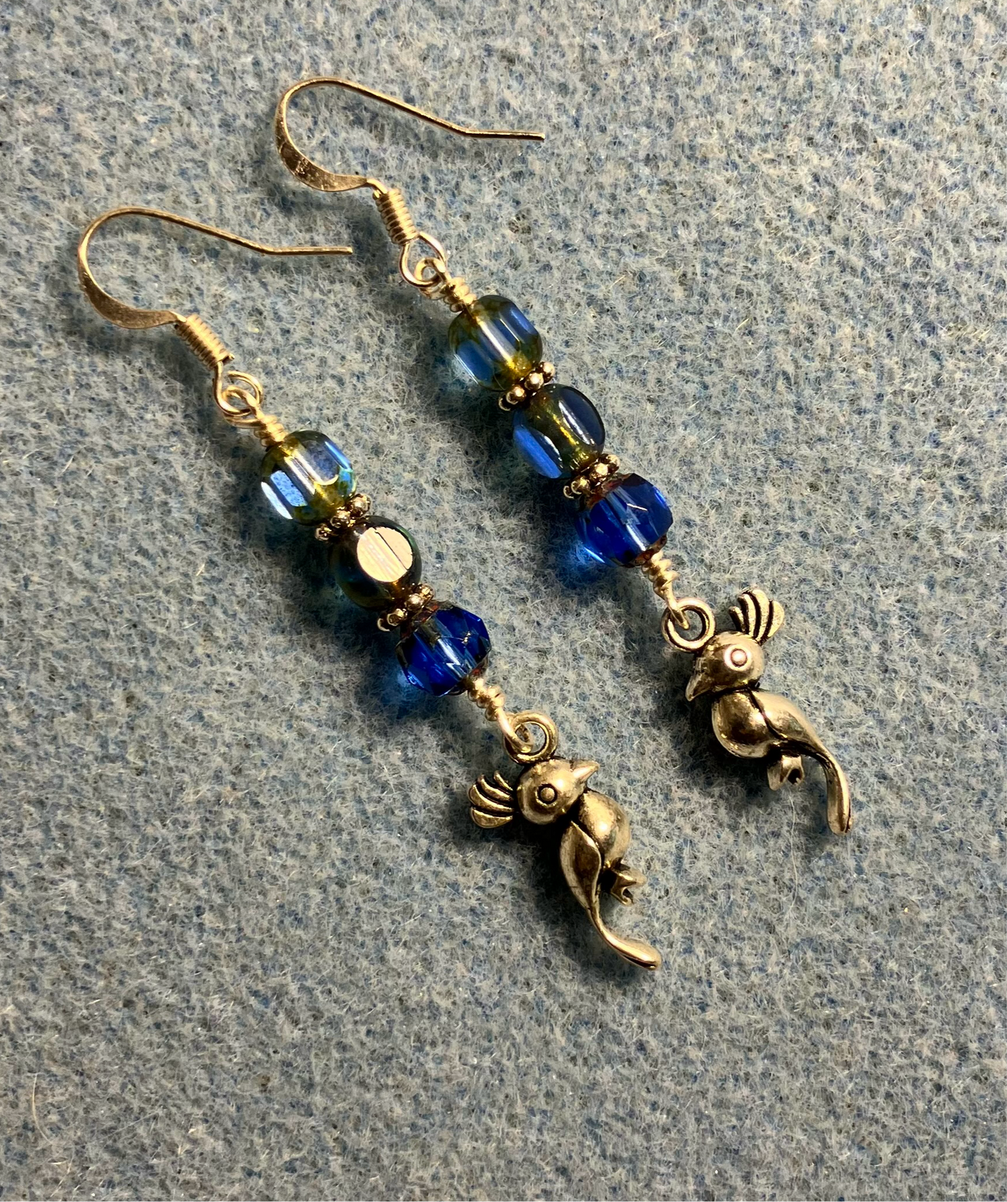 Silver parrot charm earrings adorned with blue Czech glass beads.