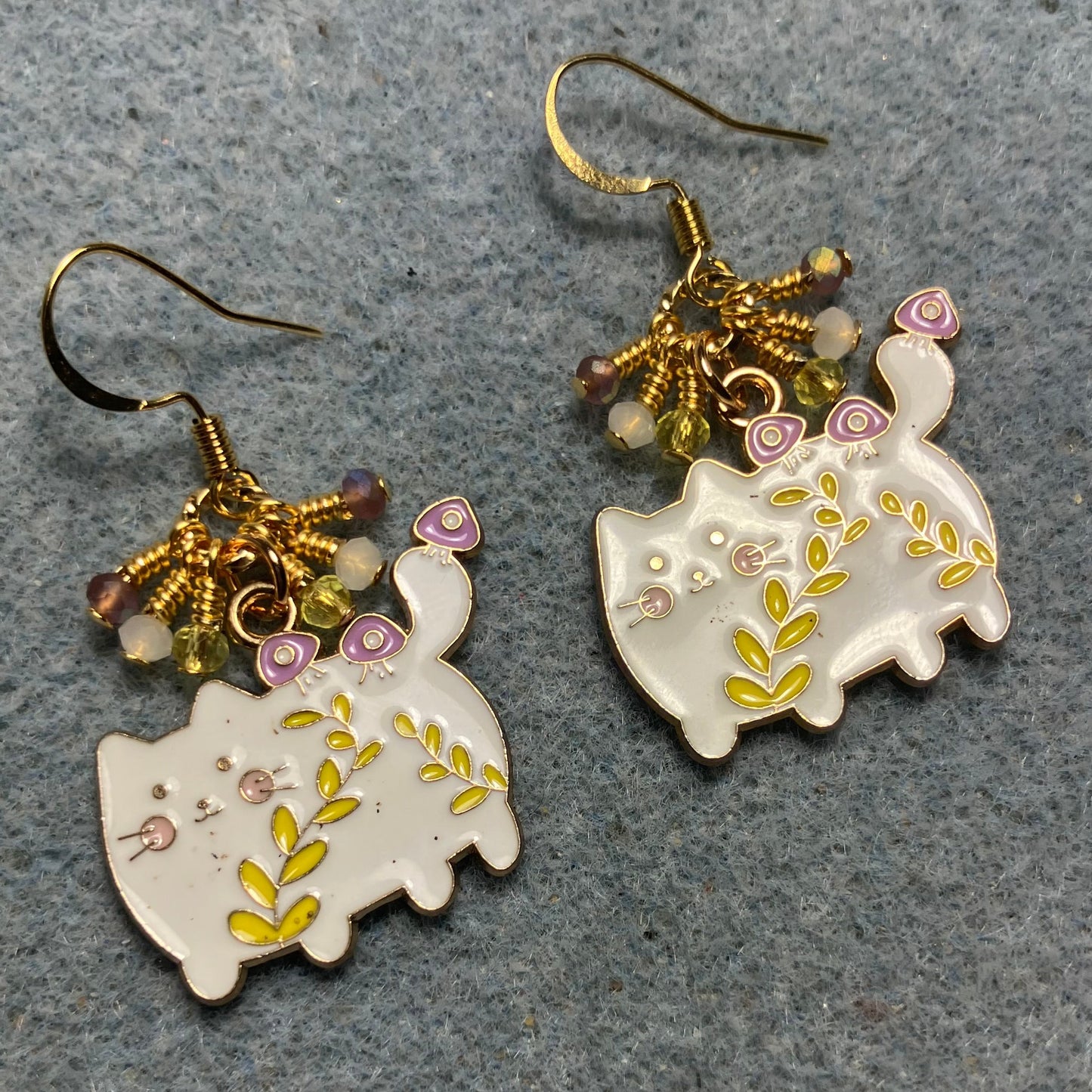 White, yellow, and violet enamel cowboy cat charm earrings adorned with tiny dangling white, yellow, and violet Chinese crystal beads.