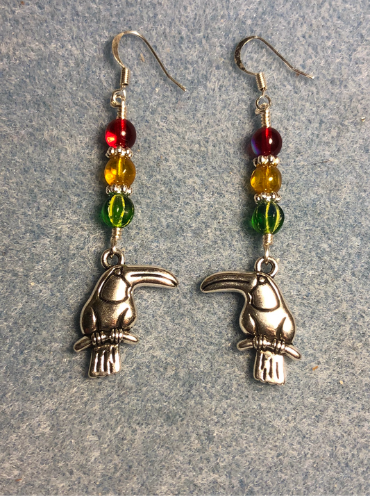 Silver toucan charm earrings adorned with green, amber, and red Czech glass beads.