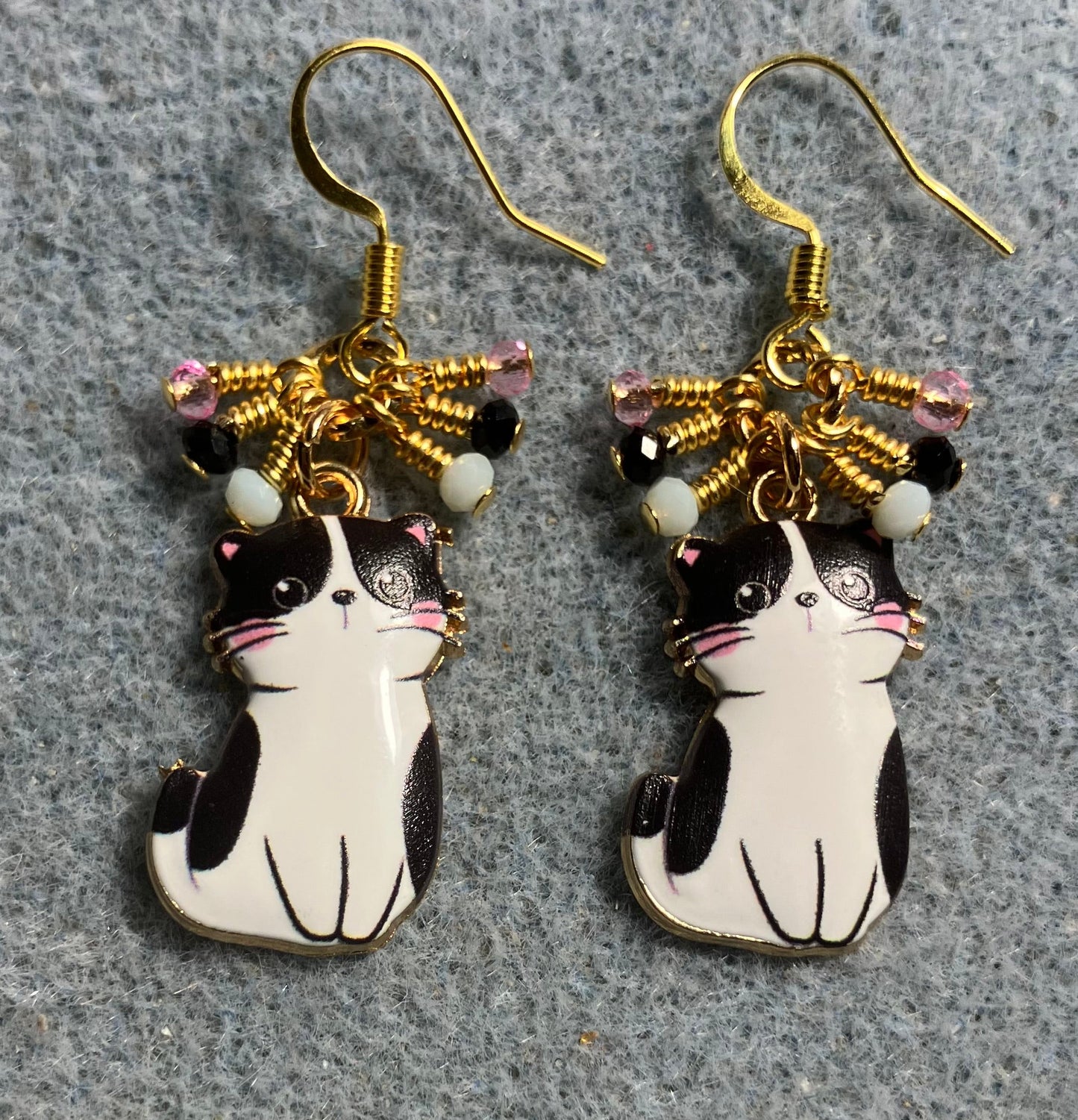 Black and white enamel cat charm earrings adorned with tiny dangling black, white, and pink Chinese crystal beads.