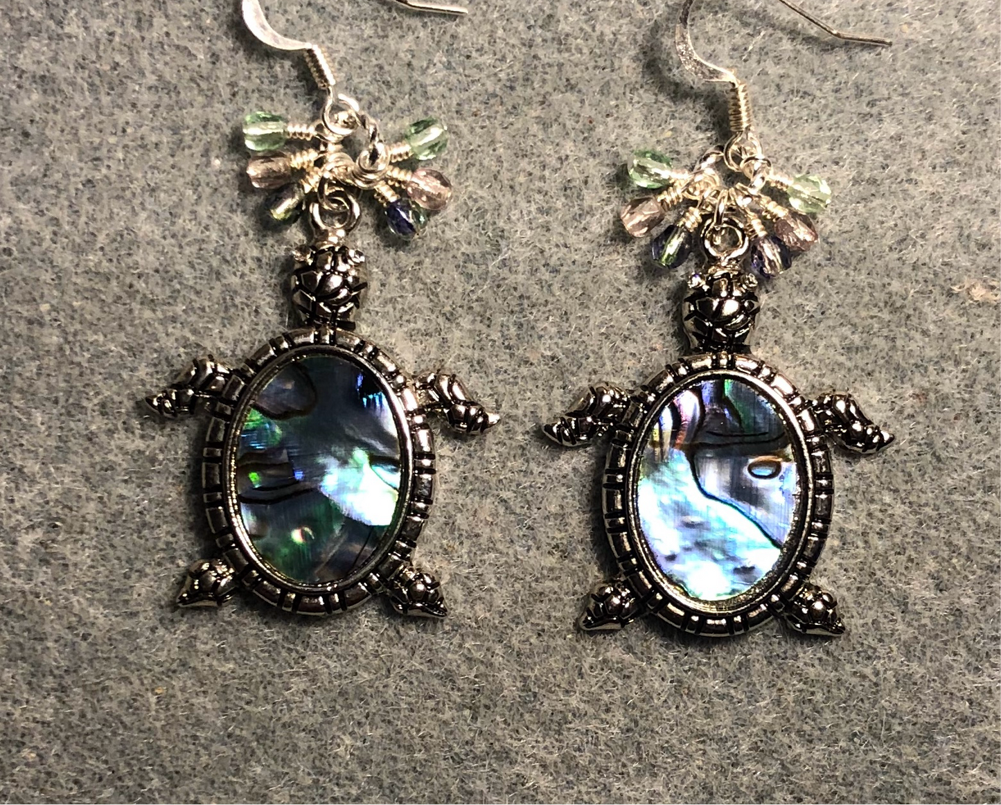 Silver and abalone turtle charm earrings adorned with small dangling green, violet, and purple Czech glass beads.