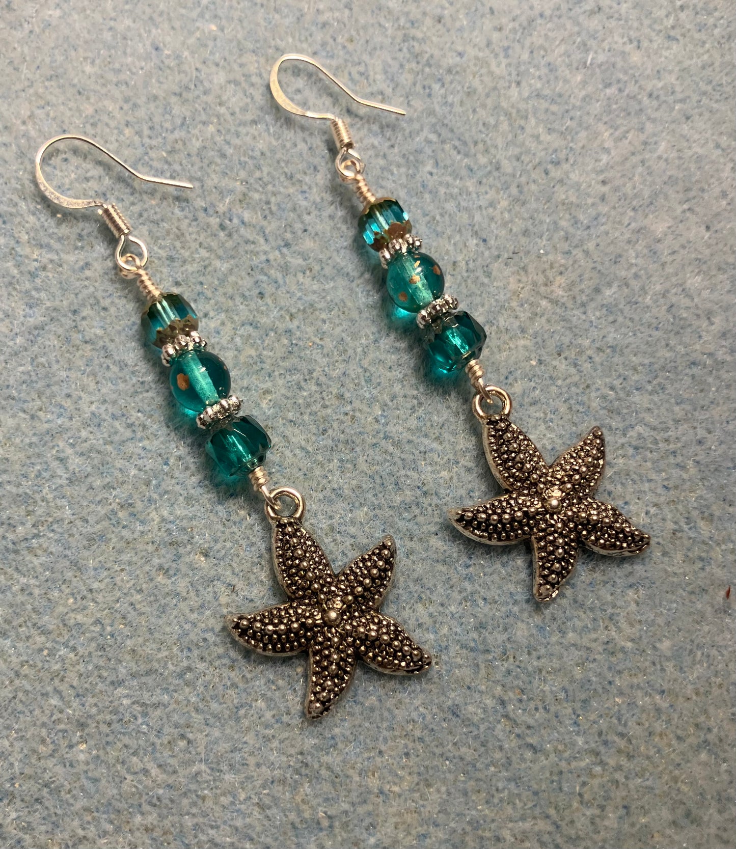 Silver starfish charm earrings adorned with teal Czech glass beads.