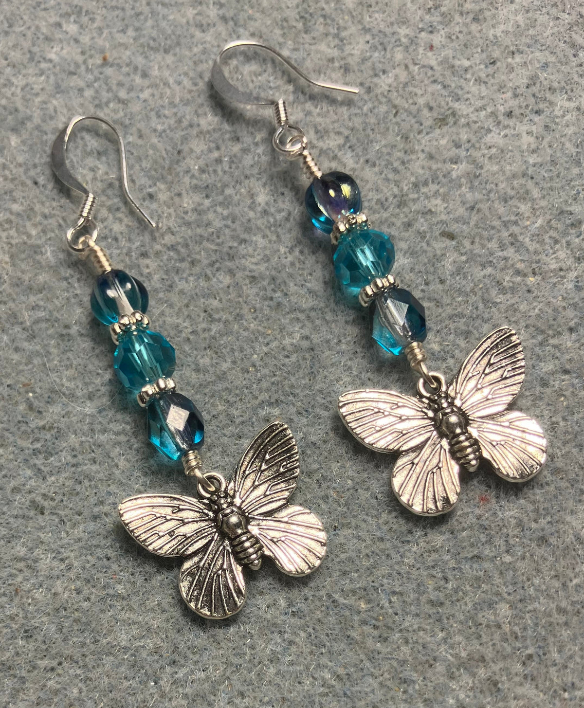 Silver butterfly charm earrings adorned with turquoise Czech glass beads.