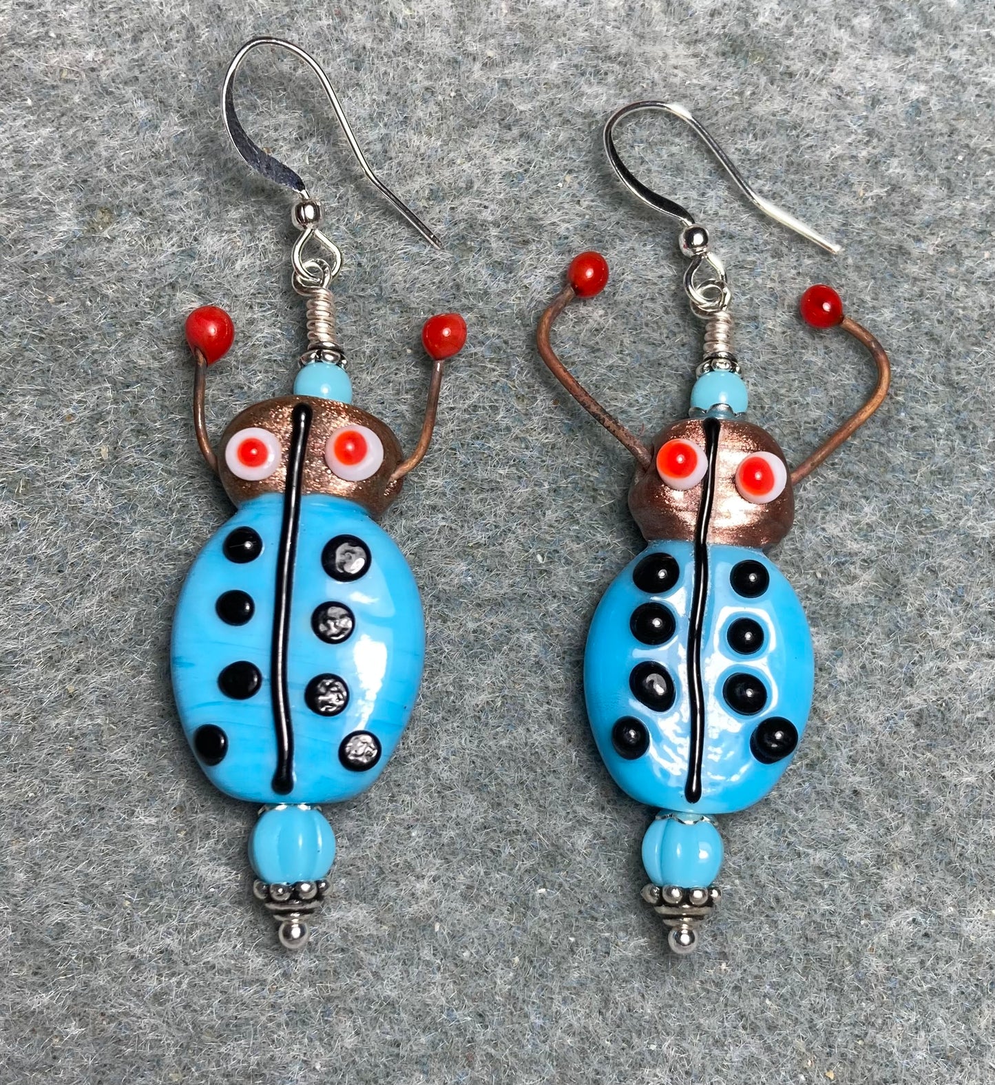 Opaque light blue, black, and red lamp work beetle bead earrings adorned with light blue Czech glass beads.