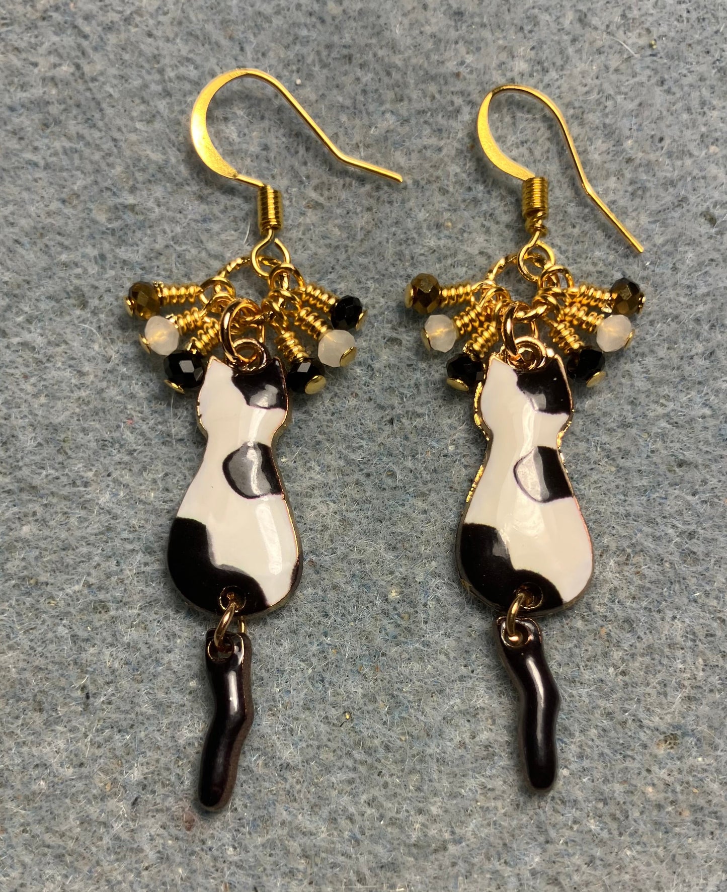 Black, white, and gold enamel cat charm earrings adorned with tiny dangling black, white, and gold Chinese crystal beads.