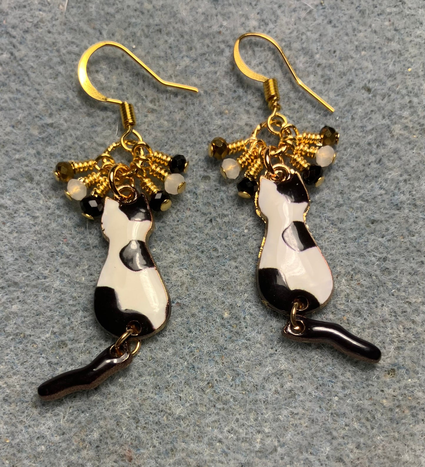 Black, white, and gold enamel cat charm earrings adorned with tiny dangling black, white, and gold Chinese crystal beads.