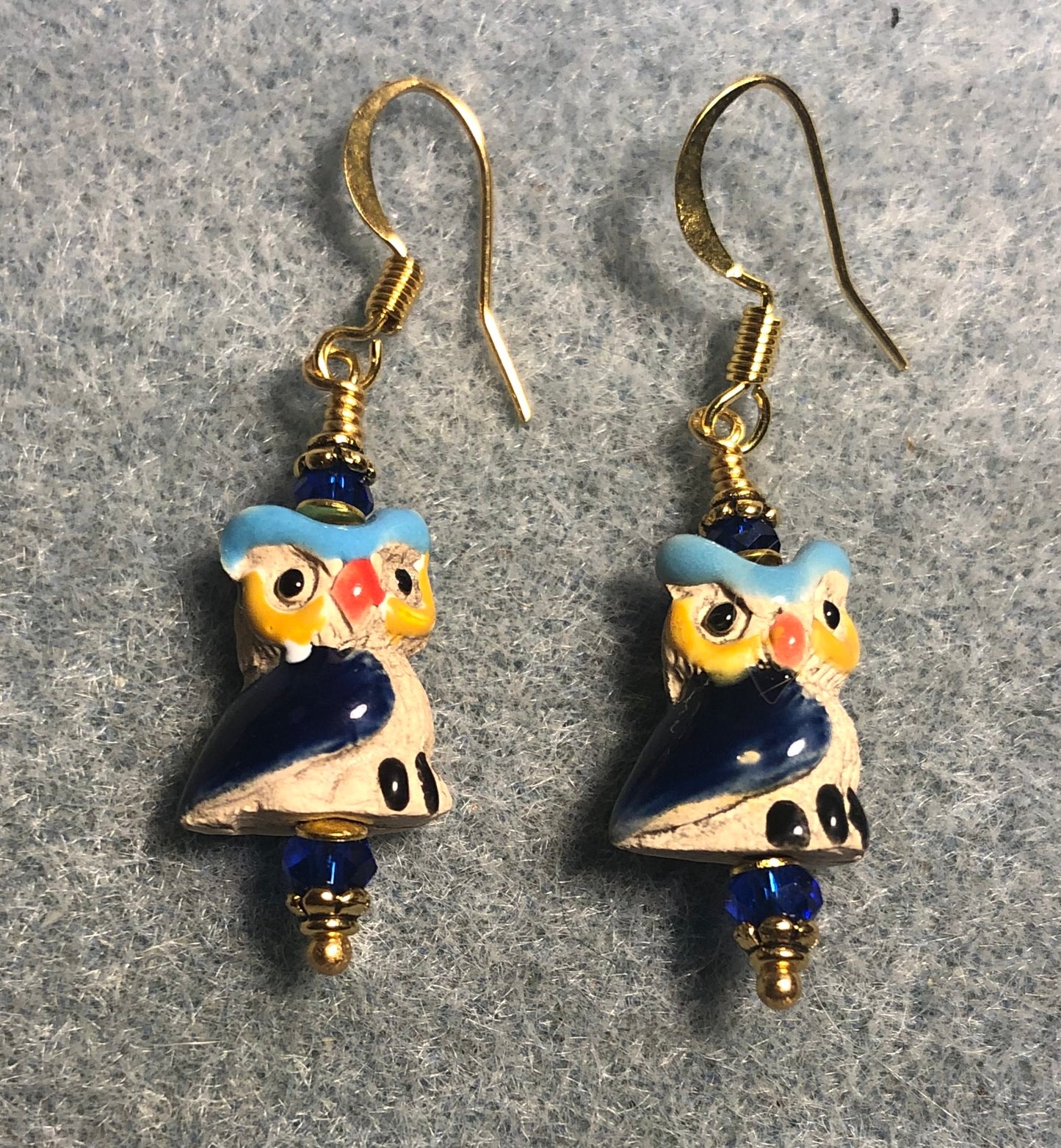 Small tan, turquoise, yellow, and dark blue ceramic owl bead earrings adorned with dark blue Chinese crystal beads.