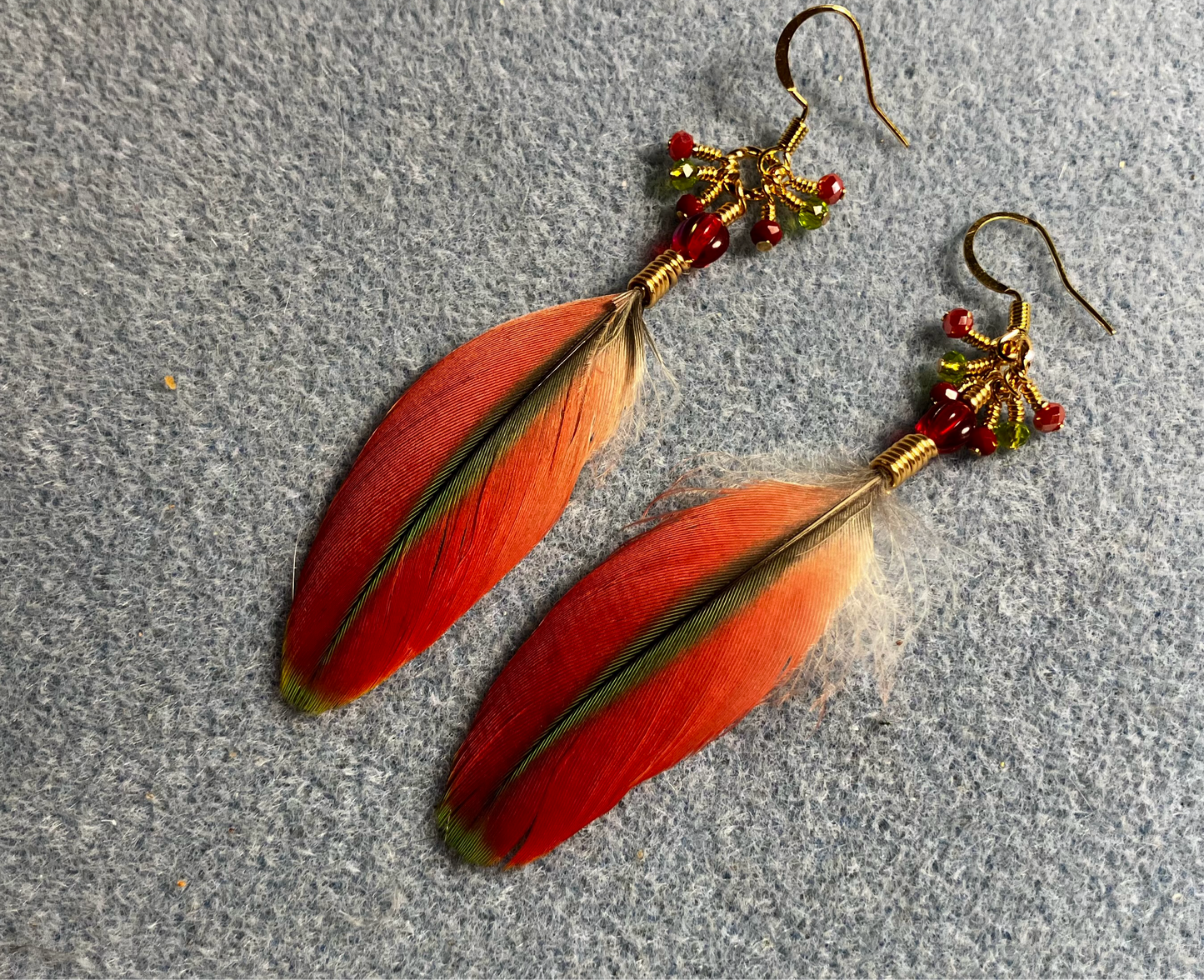 Small red and olive green Pionus feather earrings adorned with red Czech glass beads and tiny dangling red and olive green Chinese crystal beads.