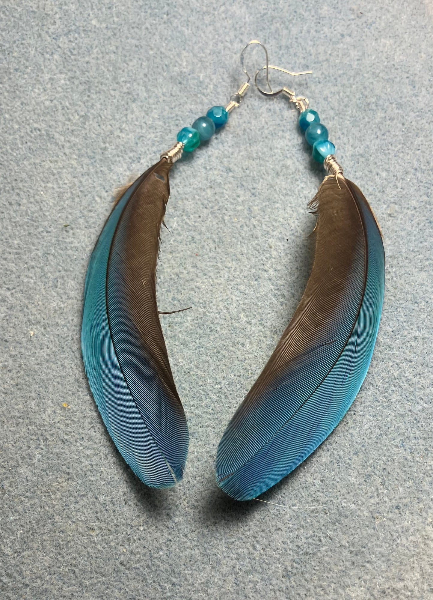 Turquoise blue macaw feather earrings adorned with turquoise Czech glass beads.