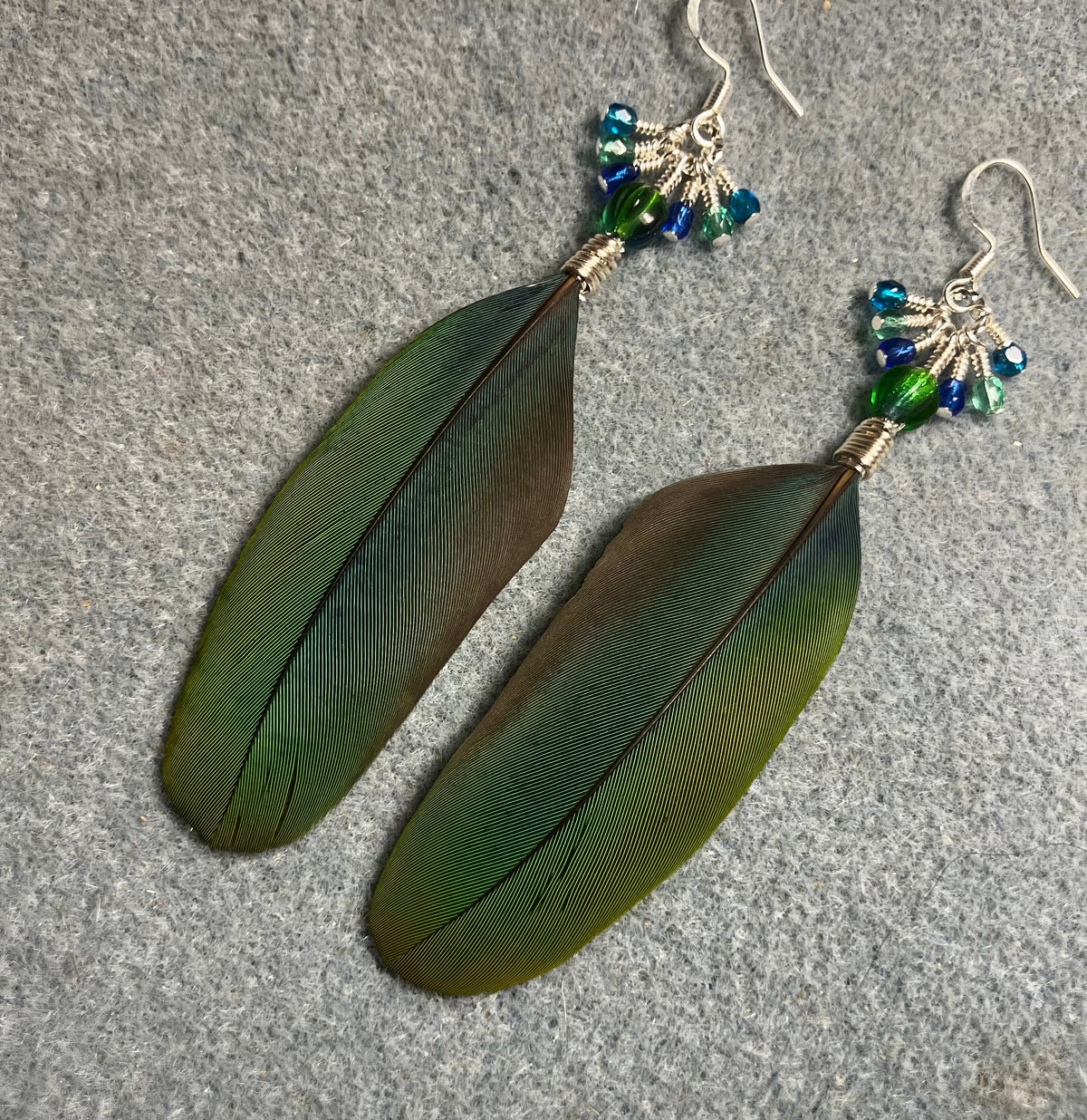 Blue and green blue headed Pionus feather earrings adorned with blue green Czech glass melon beads and small dangling blue, green, and turquoise Czech glass beads.