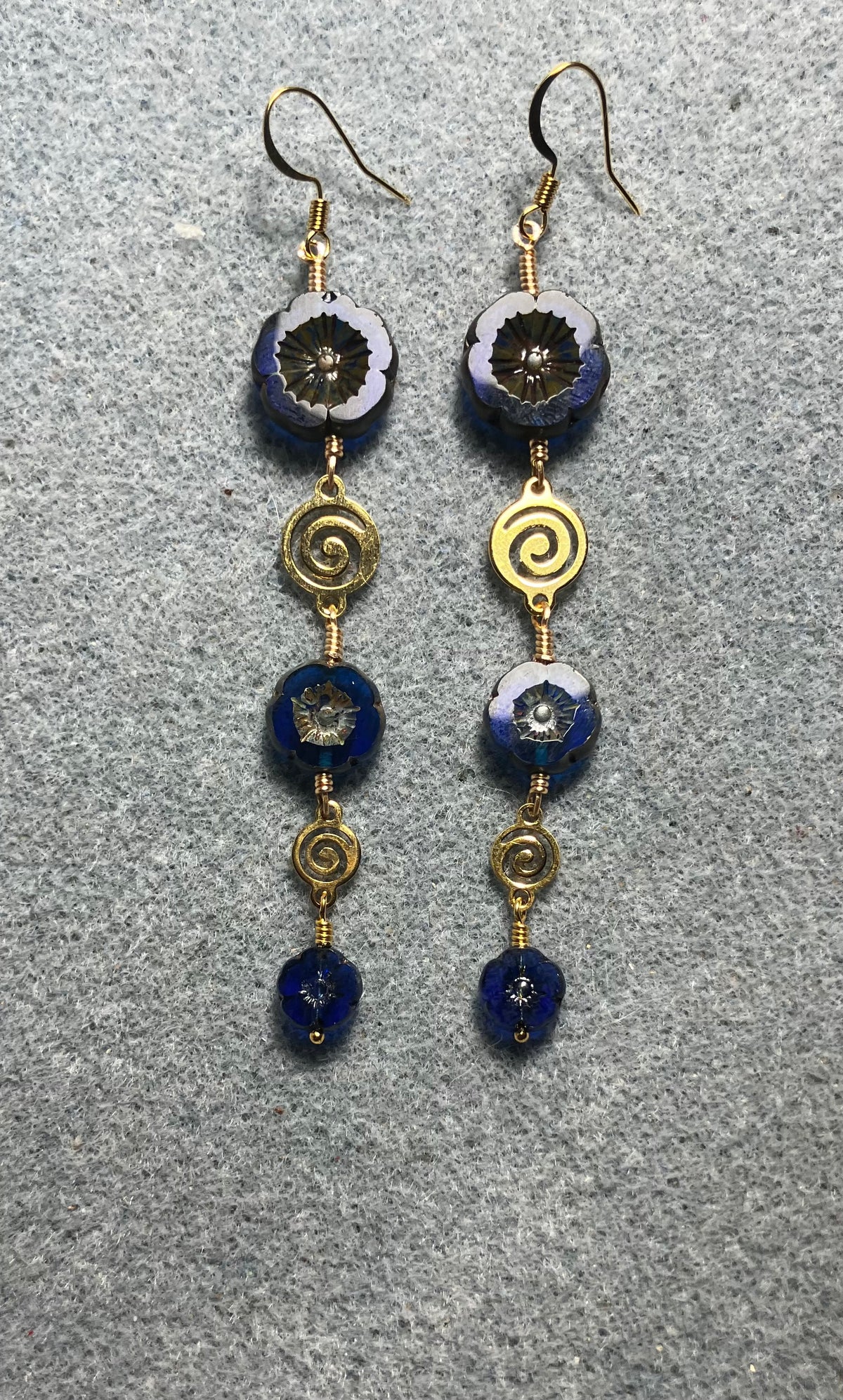 Extra long blue flower bead earrings made with three sizes of cobalt blue Czech glass pansy beads joined by gold swirly connectors.