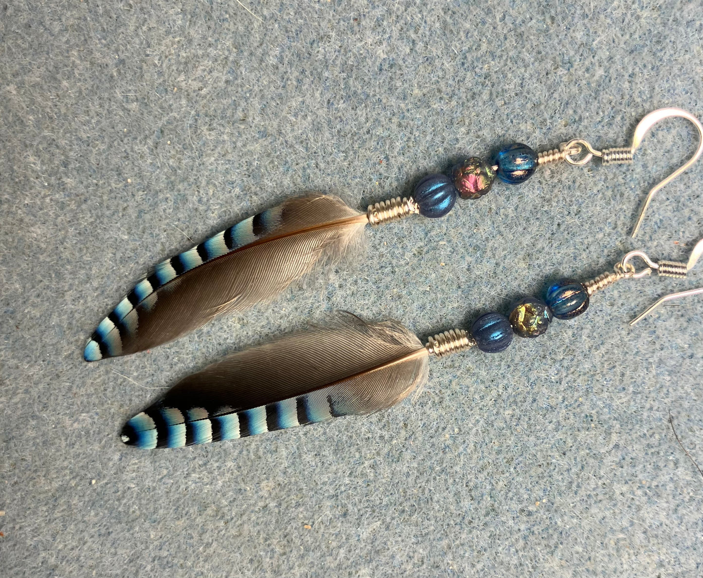 Small striped blue jay feather earrings adorned with small blue Czech glass beads.
