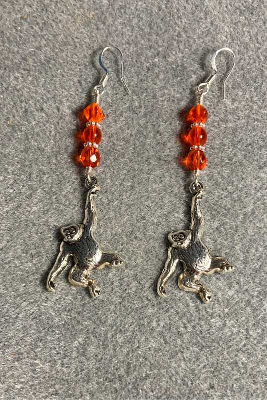 Long silver orangutan charm earrings adorned with orange Czech glass beads.