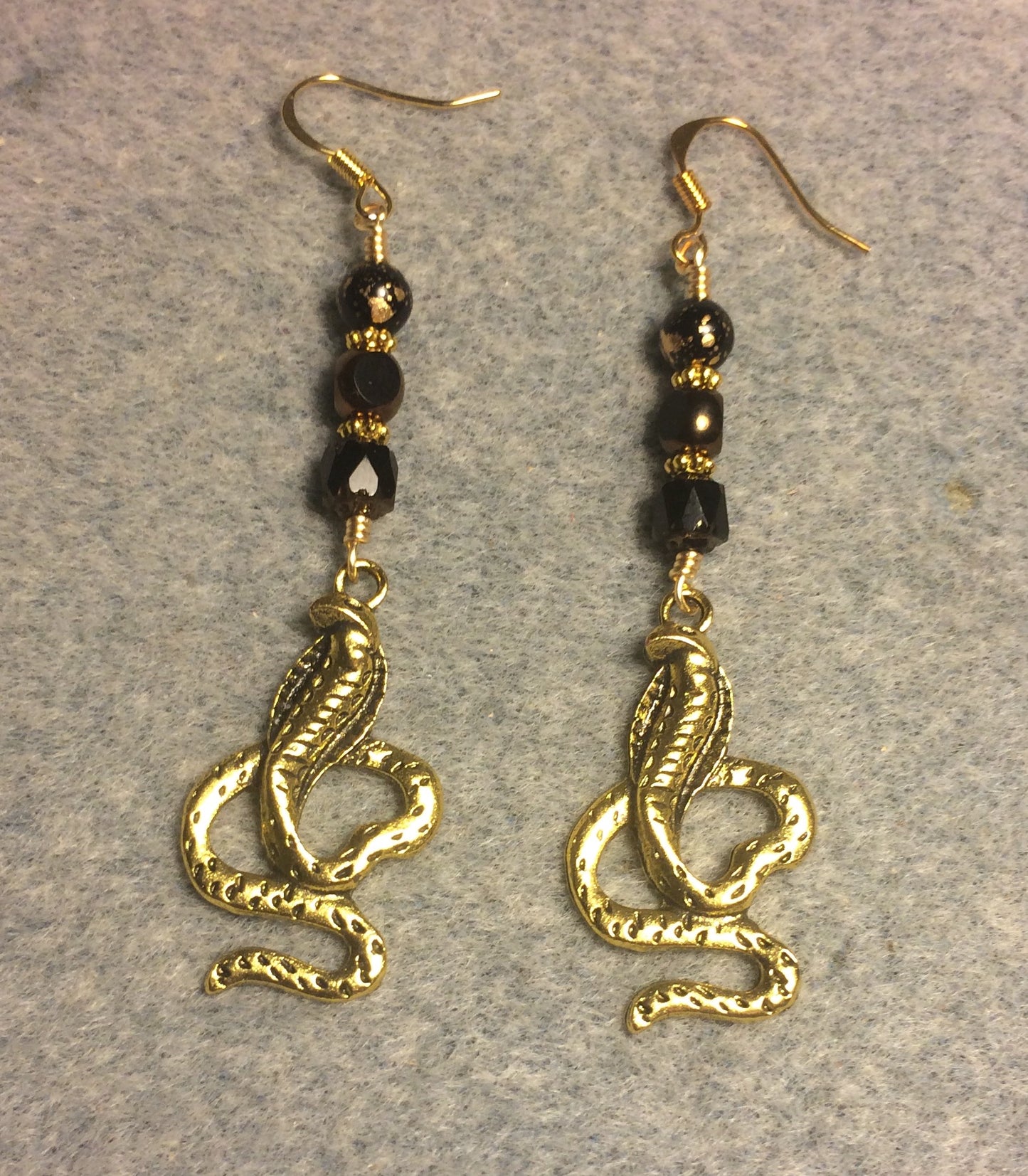 Long gold cobra charm earrings adorned with black Czech glass beads.