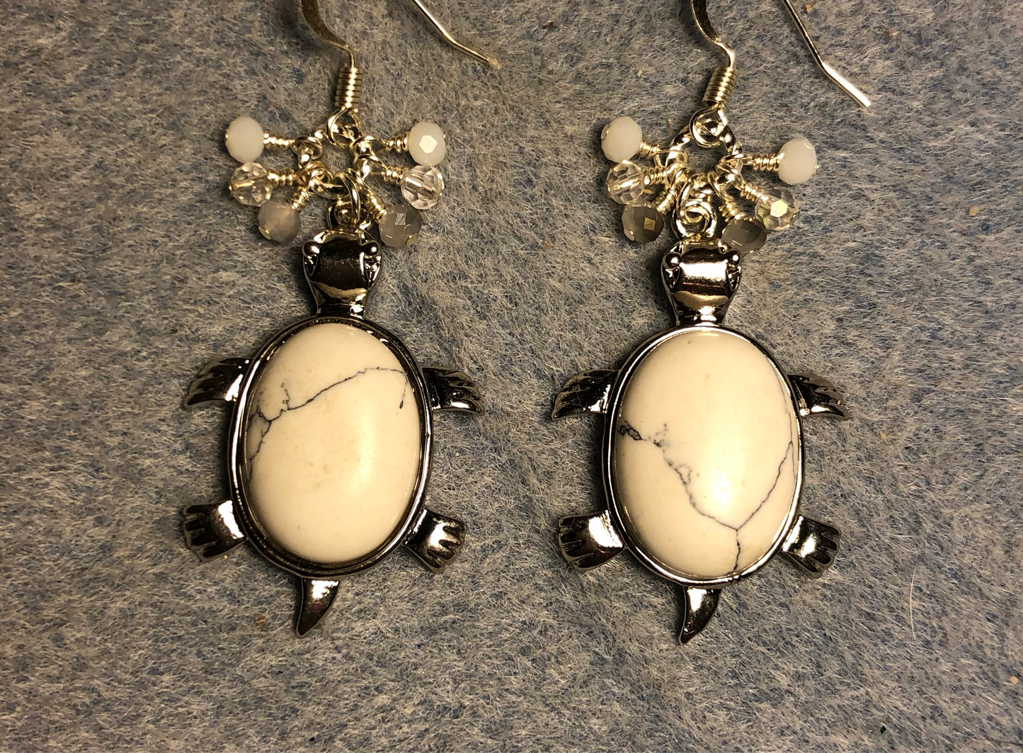 Large silver and white howlite gemstone turtle charm earrings adorned with small dangling white, gray, and silver Czech glass beads.