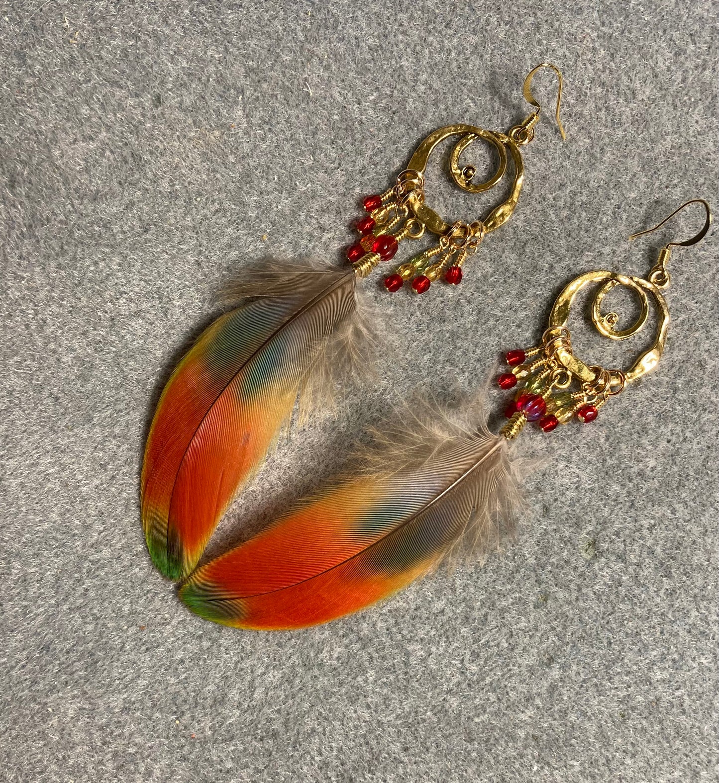 Red, yellow, and green macaw feather earrings attached to gold chandelier findings and adorned with red Czech glass melon beads and small dangling red, amber, and green Czech glass beads.