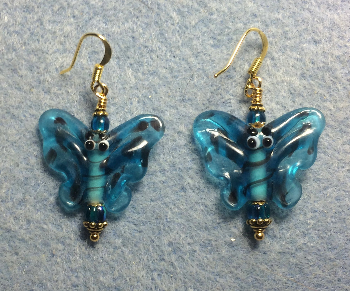 Dark turquoise lamp work butterfly bead earrings adorned with turquoise Czech glass beads.