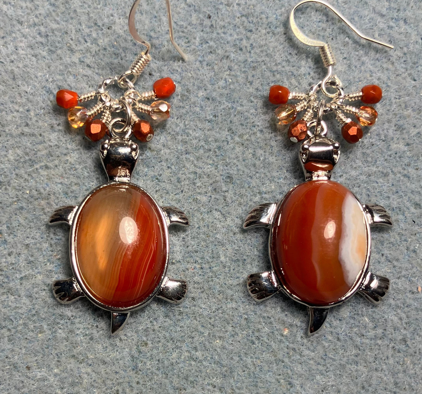Large silver and red agate gemstone turtle charm earrings adorned with small dangling orange Czech glass beads.