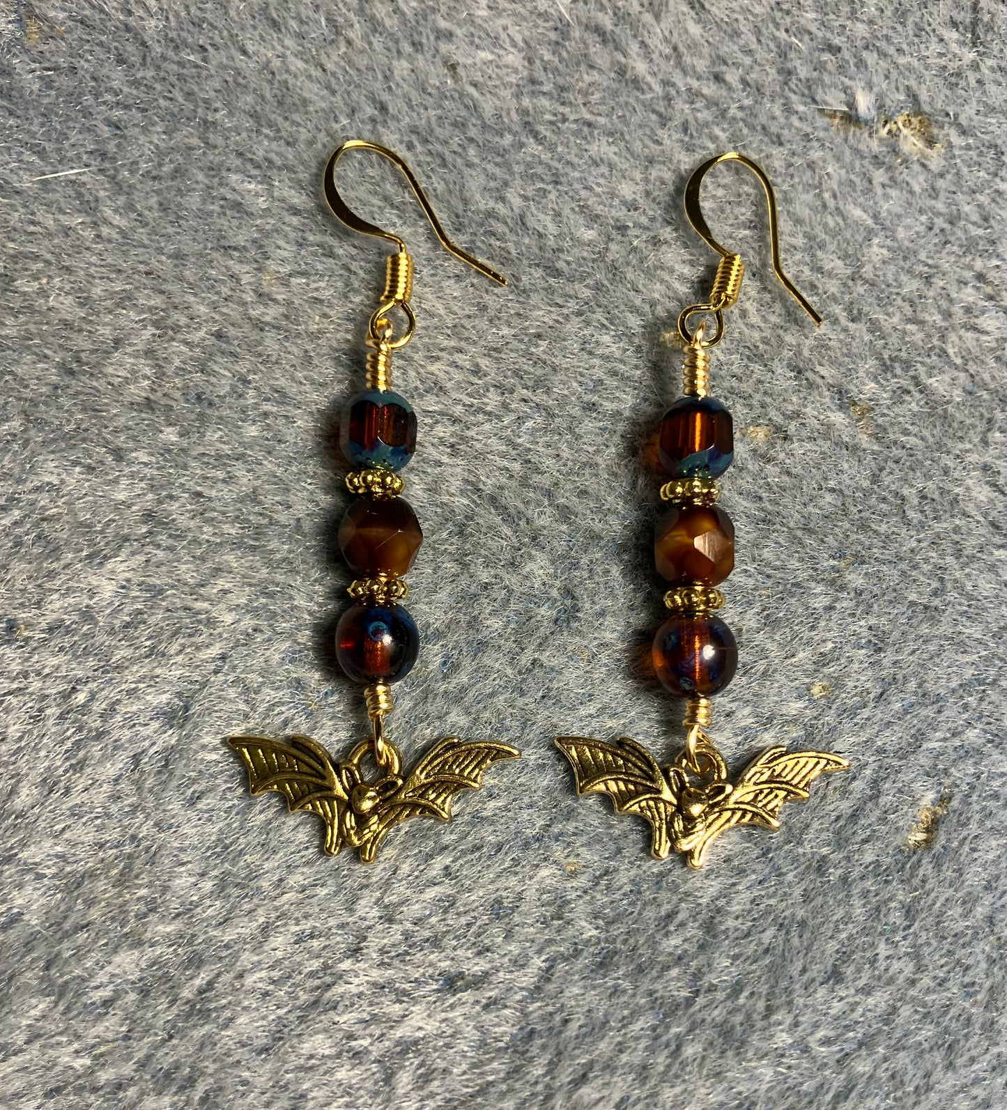 Small gold bat charm earrings adorned with blue Czech glass beads