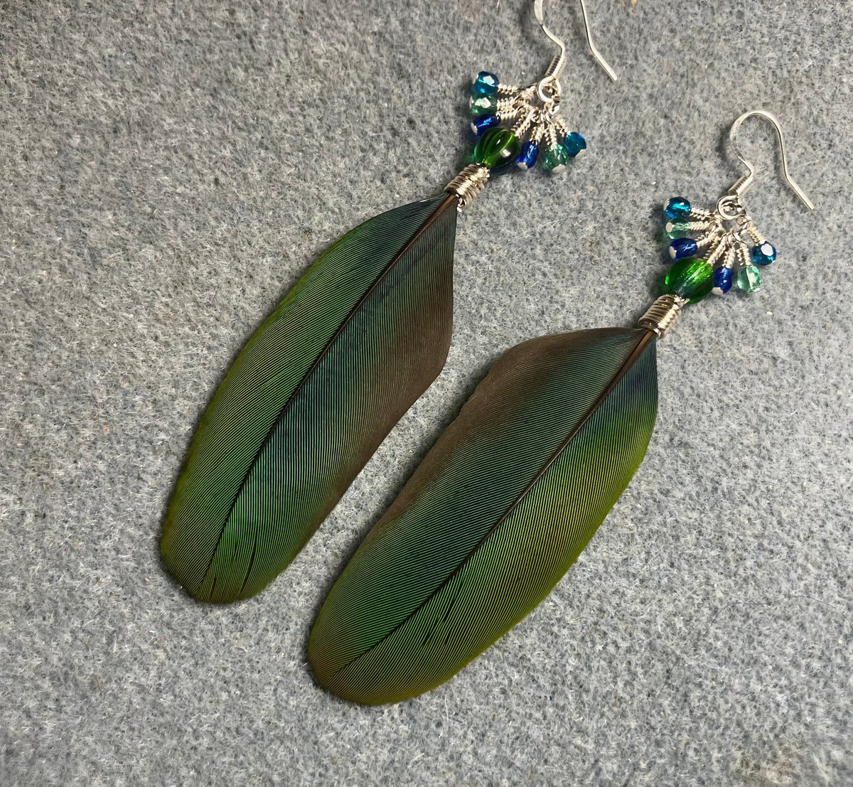 Blue and green blue headed Pionus feather earrings adorned with blue green Czech glass melon beads and small dangling blue, green, and turquoise Czech glass beads.