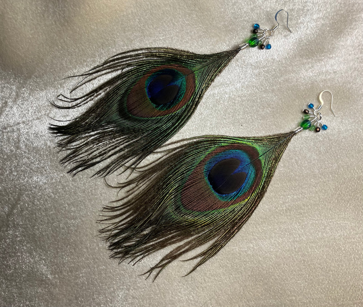 Peacock eye feather earrings adorned with small dangling green, brown, and teal Czech glass beads.