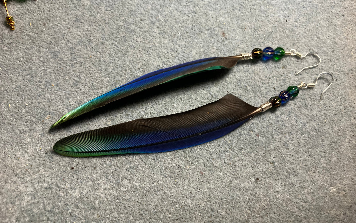 Rare iridescent blue and green Pionus parrot feather earrings adorned with blue and green Czech glass beads.