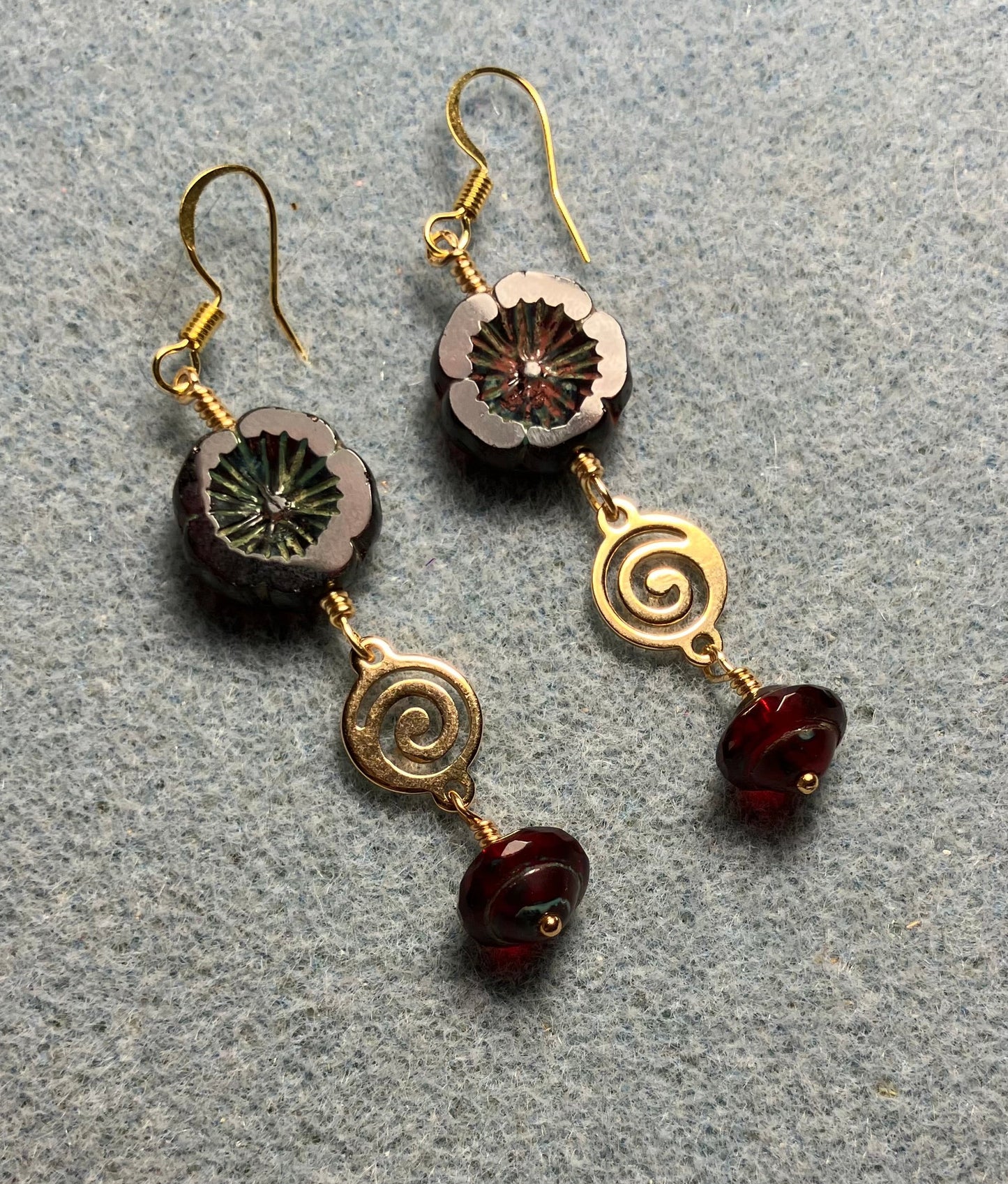 Dark red Czech glass pansy bead earrings adorned with gold swirly connectors and dark red Czech glass Saturn beads.