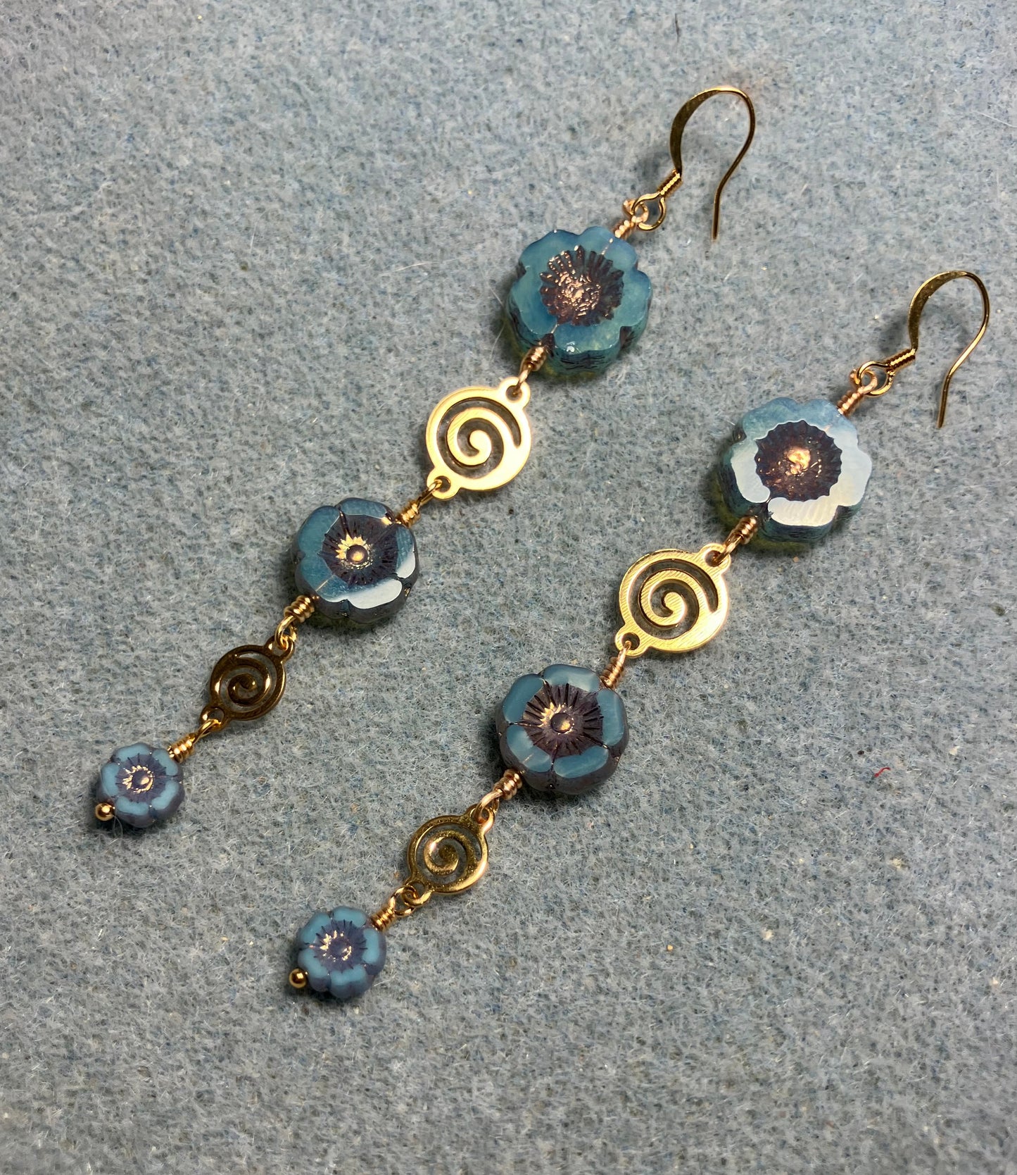 Extra long blue and copper flower bead earrings made with three sizes of blue and copper Czech glass pansy beads joined by gold swirly connectors.