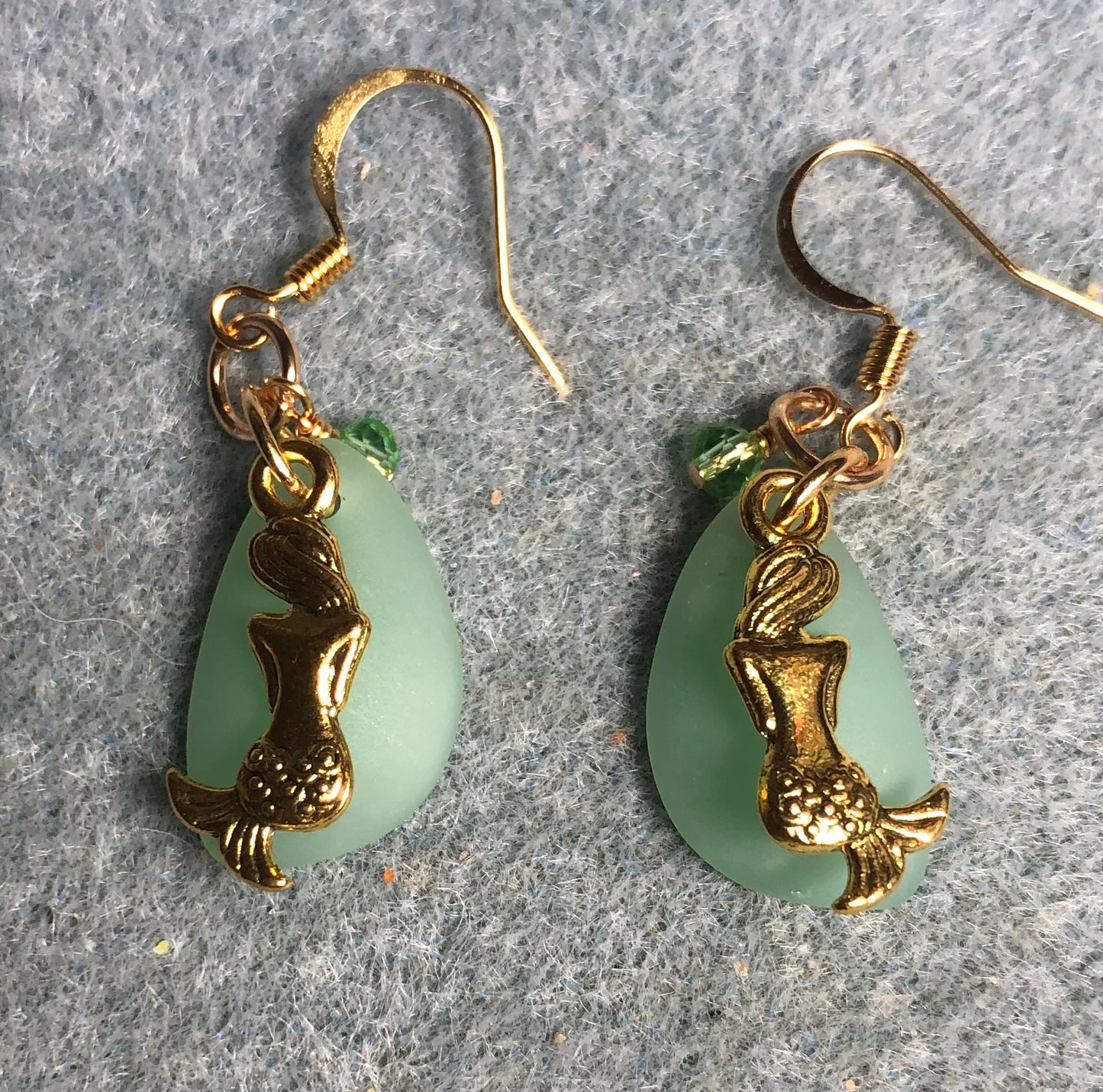 Small light green sea glass pendant bead earrings adorned with small gold mermaid charms and small light green Chinese crystal beads.