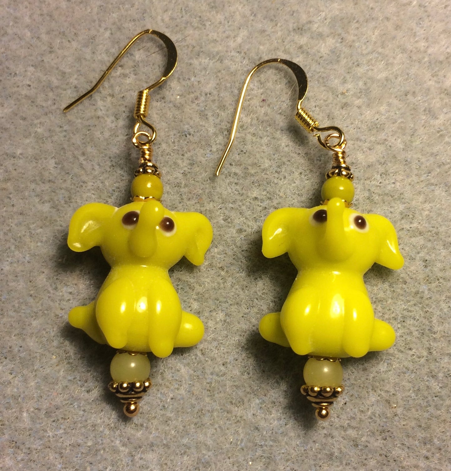 Opaque yellowish green lamp work sitting elephant bead earrings adorned with yellowish green Czech glass beads.