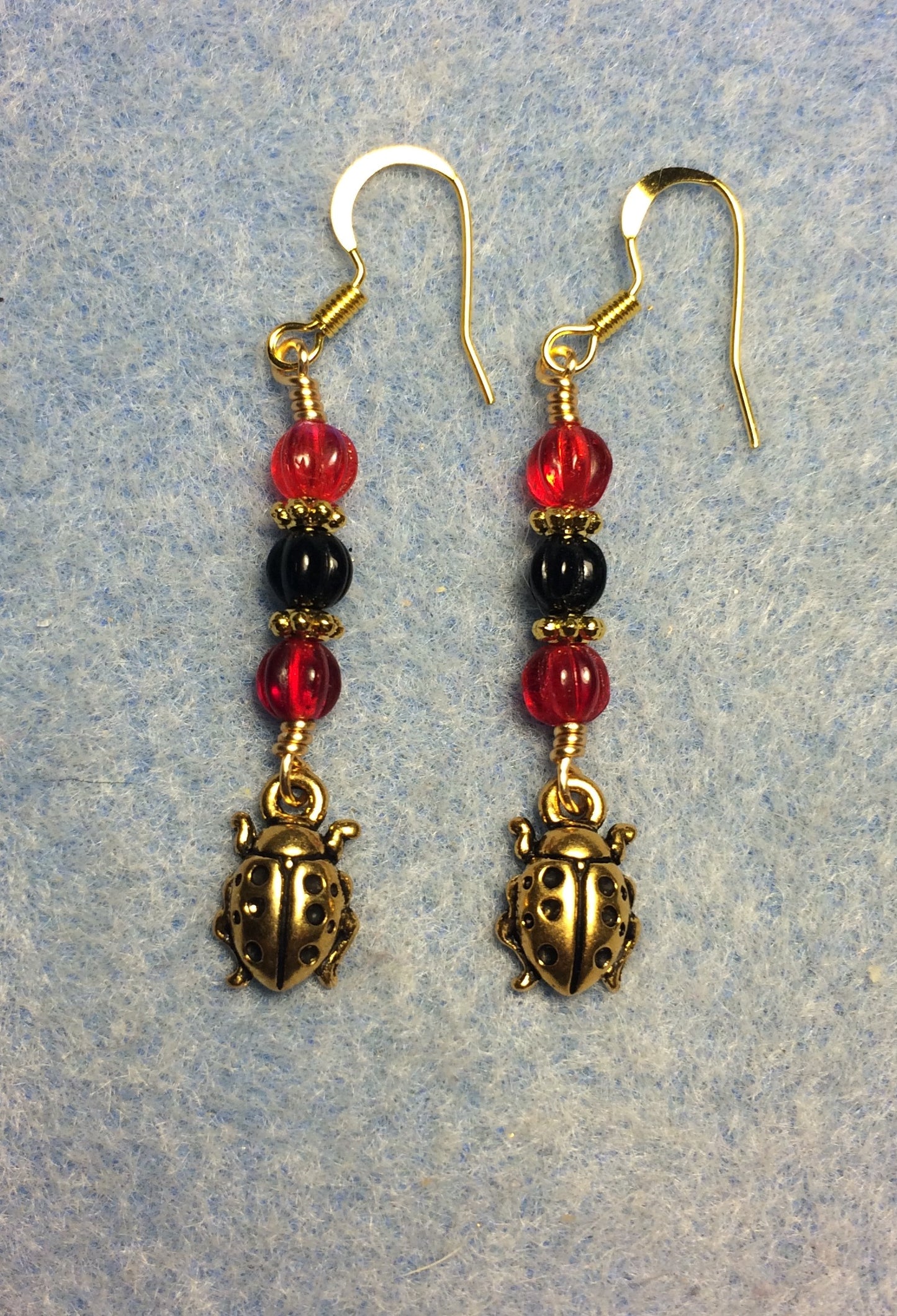 Gold ladybug charm earrings adorned with red and black Czech glass beads.