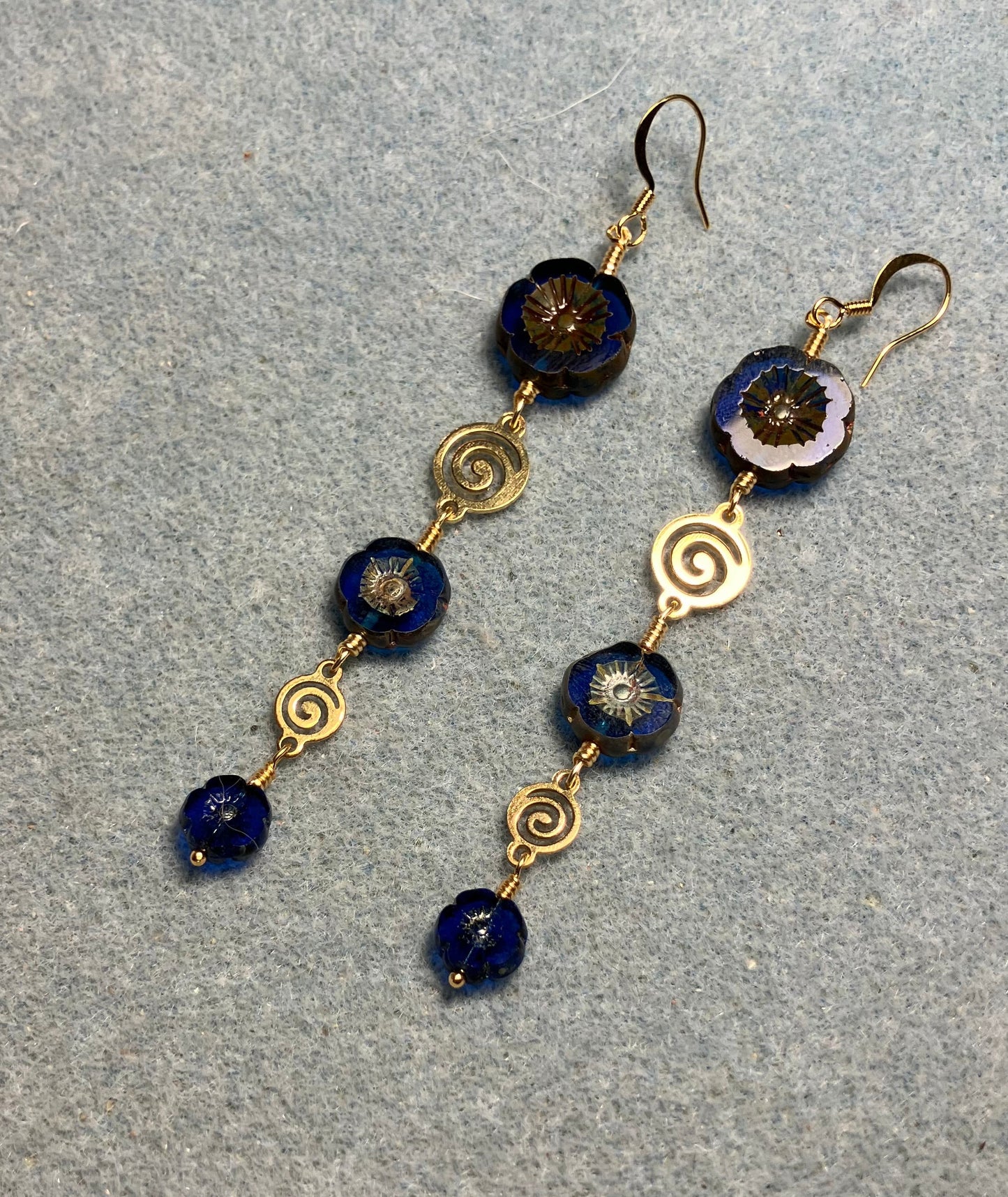 Extra long blue flower bead earrings made with three sizes of cobalt blue Czech glass pansy beads joined by gold swirly connectors.
