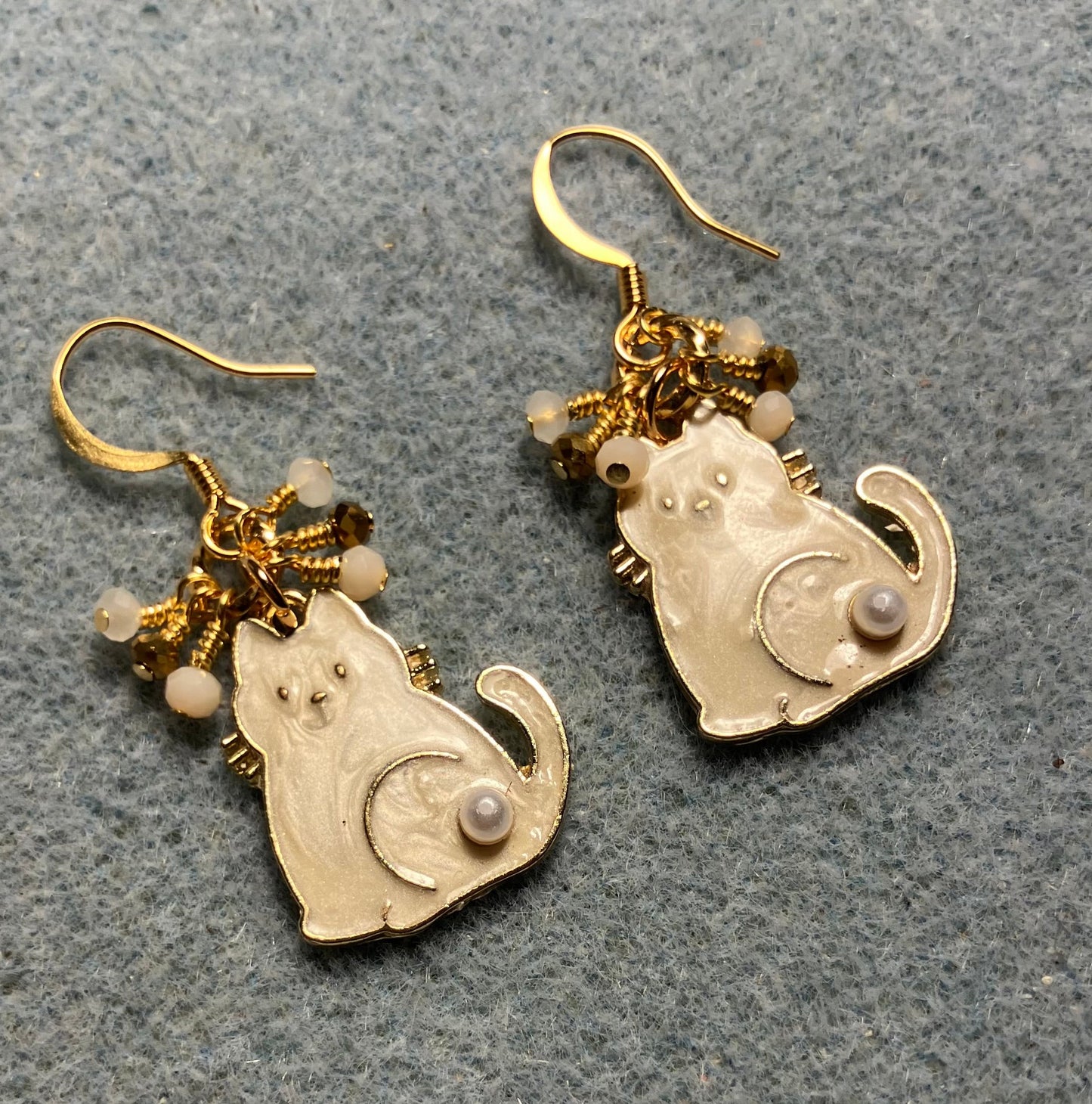 White and gold enamel and pearl cat charm earrings adorned with tiny dangling white and gold Chinese crystal beads.
