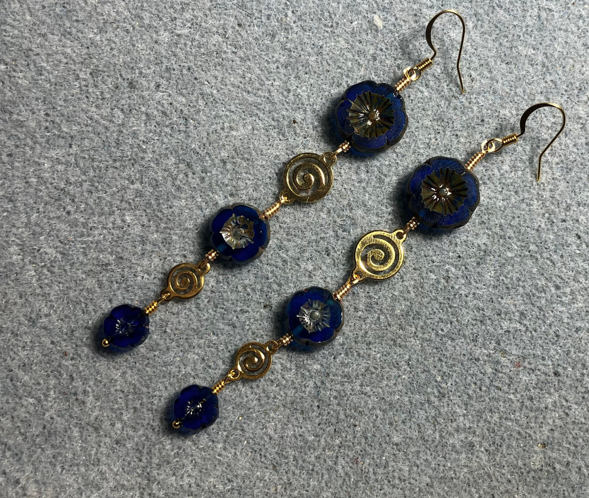 Extra long blue flower bead earrings made with three sizes of cobalt blue Czech glass pansy beads joined by gold swirly connectors.