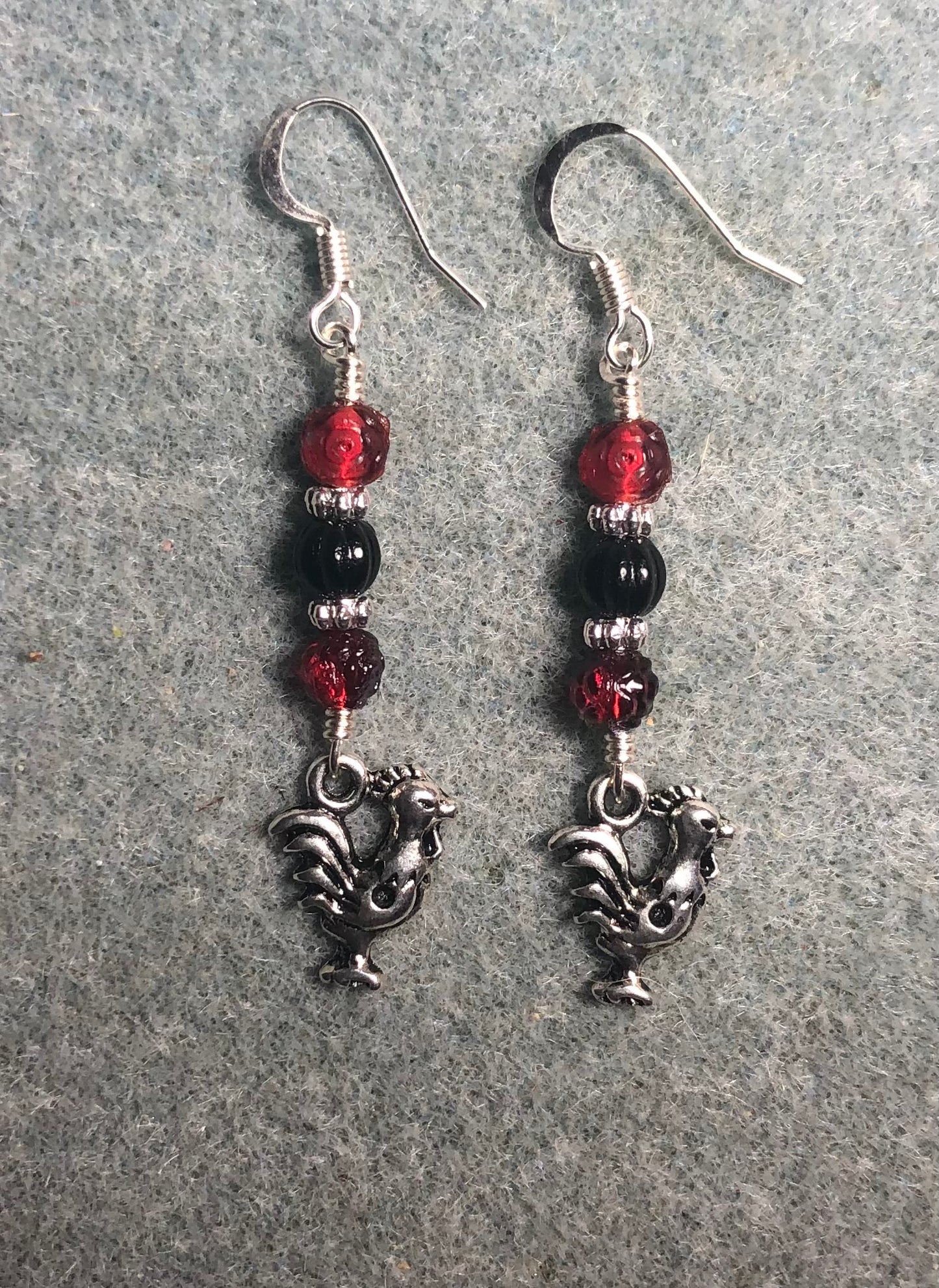 Silver rooster charm earrings adorned with red and black Czech glass beads.