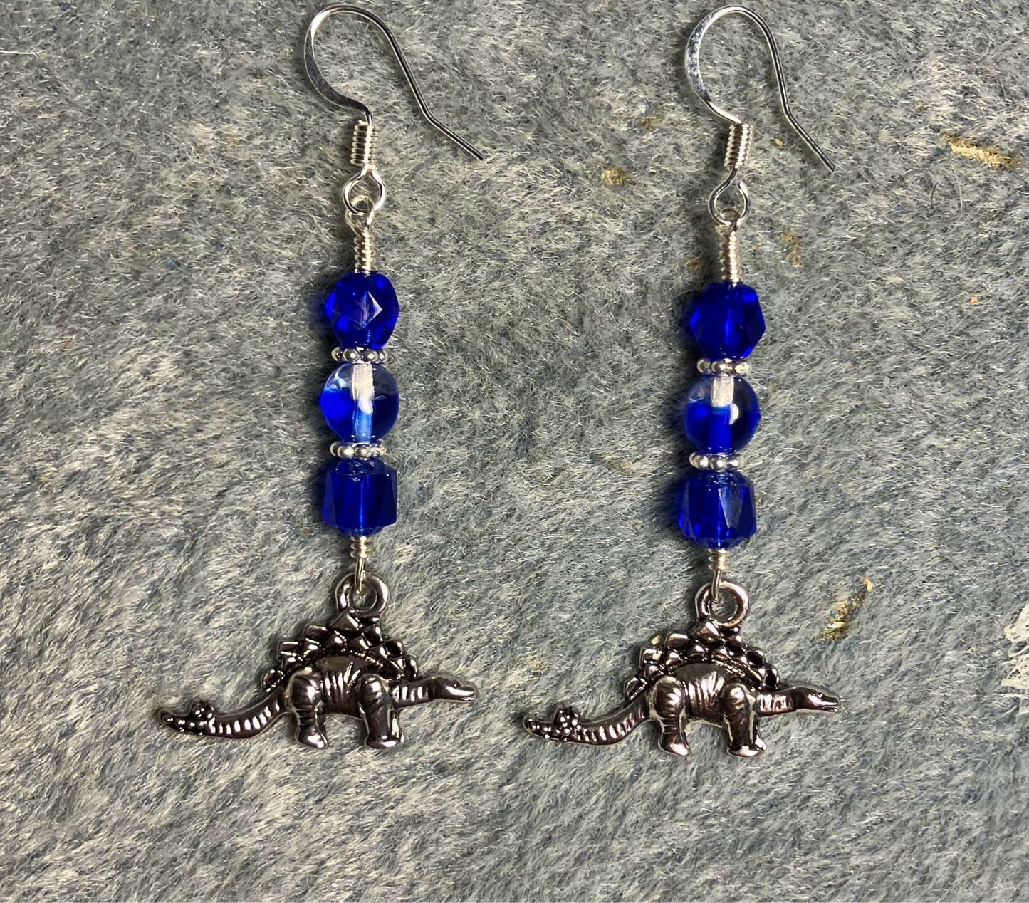 Silver stegosaurus charm earrings adorned with dark blue Czech glass beads.