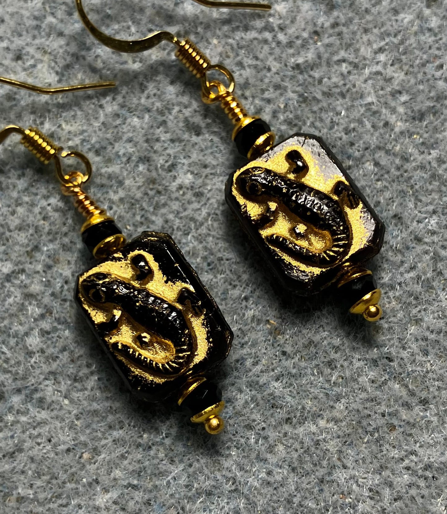 Small black and gold Czech glass lizard bead earrings adorned with black Chinese crystal beads.
