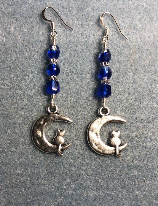 Silver cat sitting on a quarter moon charm earrings adorned with dark blue Czech glass beads