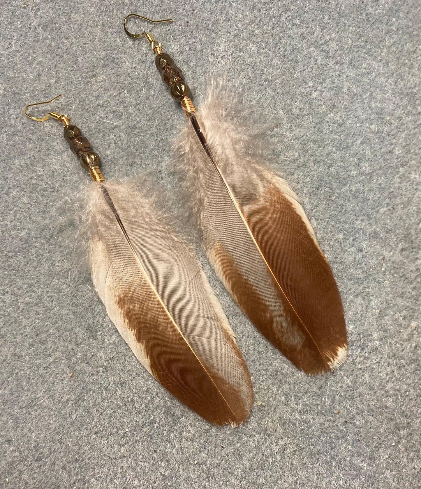 Brown and white chicken feather earrings adorned with gold Czech glass beads.