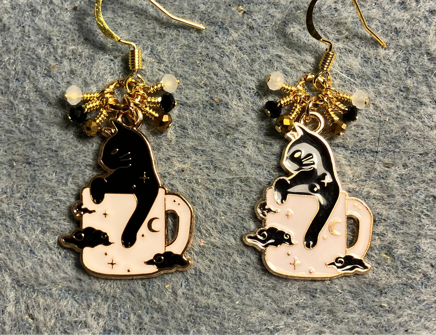 Black and white enamel cat charm earrings adorned with tiny dangling black, gold, and white Chinese crystal beads.