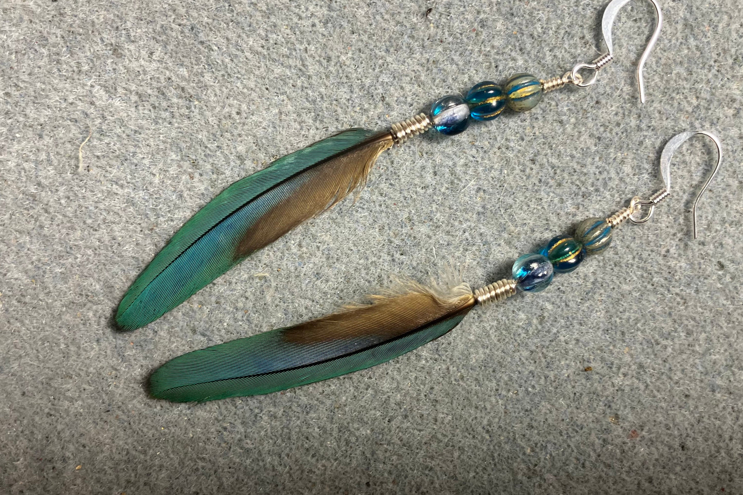 Slender turquoise blue and gold macaw feather earrings adorned with turquoise Czech glass beads.