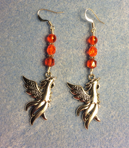 Long silver rising phoenix charm earrings adorned with orange Czech glass beads