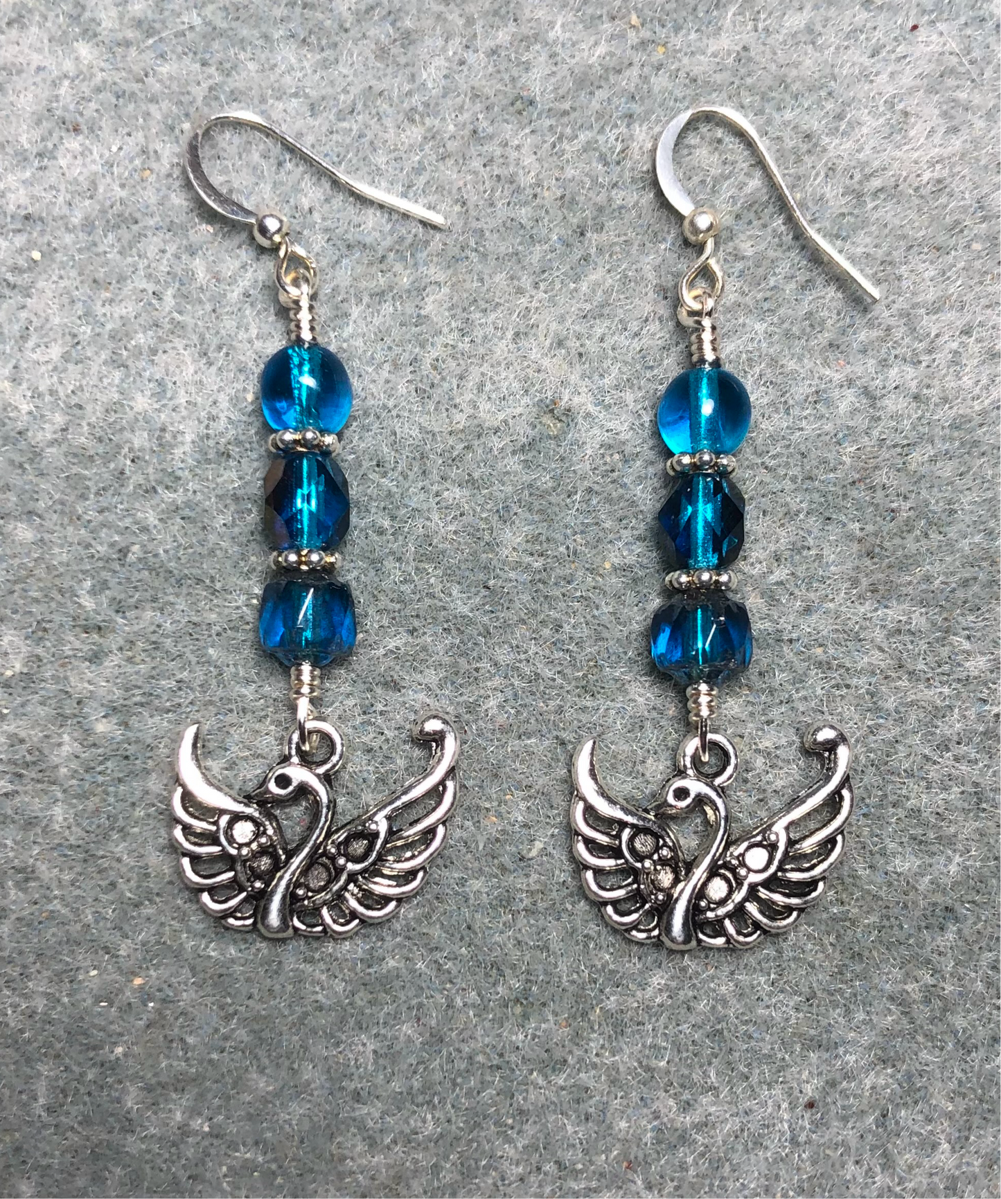 Silver swan charm earrings adorned with dark turquoise Czech glass beads.